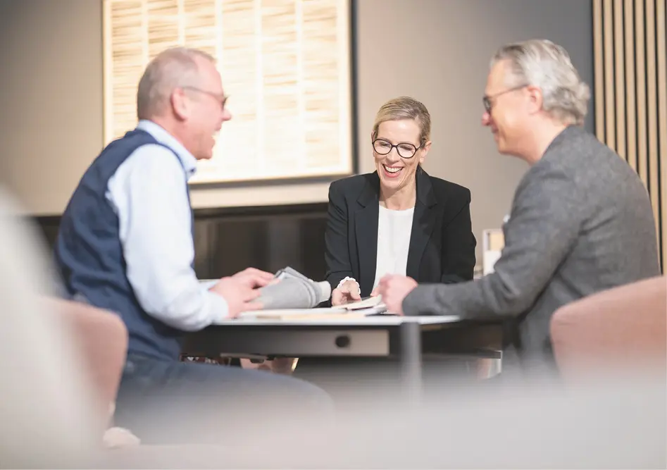 Drei Personen sitzen am Tisch und betrachten Stoffmuster und Unterlagen während eines Beratungsgesprächs im Möbelhaus